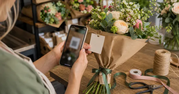 Florist using a phone to scan a blank tag on a wrapped bouquet at the packing bench