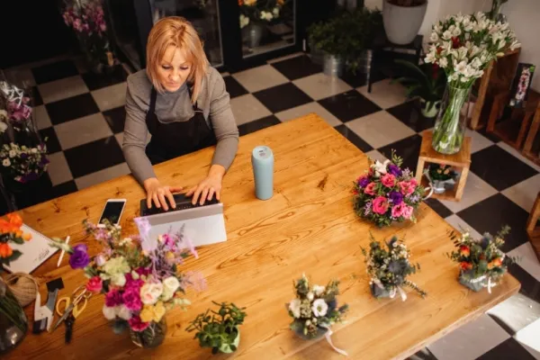 Florist workroom table with flowers, a laptop and planning notes