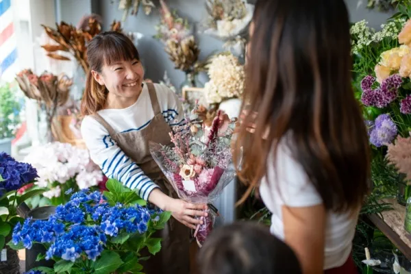Florist handing a wrapped bouquet to a customer in a flower shop