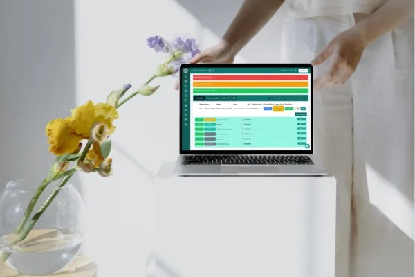 Laptop showing a florist order dashboard beside flowers in a vase