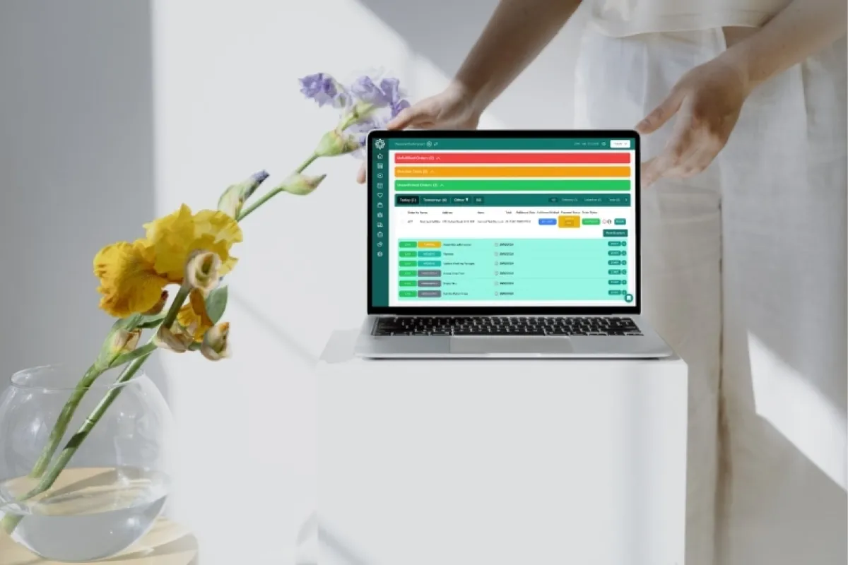 Laptop showing a florist order dashboard beside flowers in a vase
